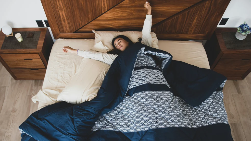 Mujer sonriente estirándose en una cama cómoda al despertar, representando un descanso reparador y un colchón de calidad.