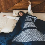 Mujer sonriente estirándose en una cama cómoda al despertar, representando un descanso reparador y un colchón de calidad.